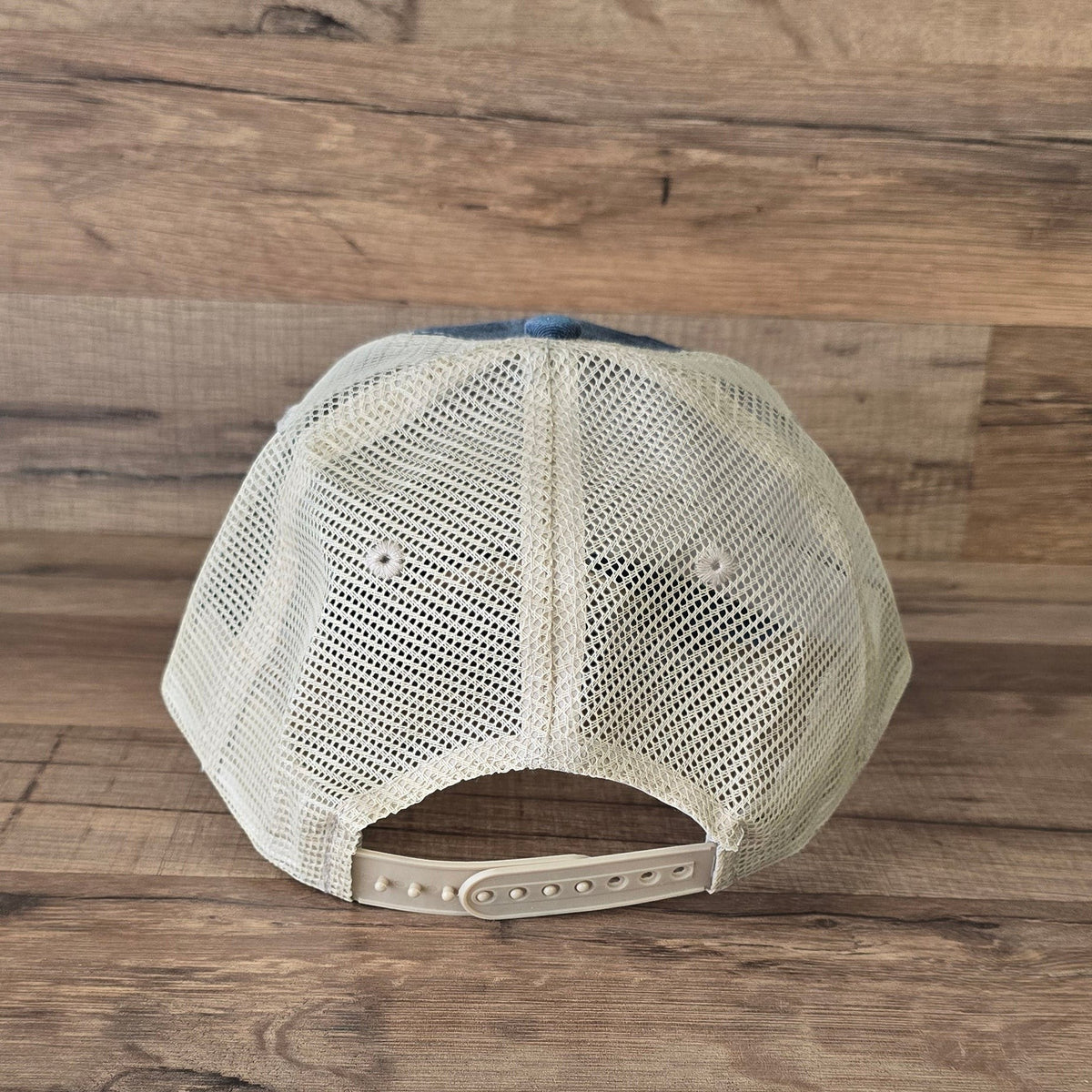 Allen's Bootery trucker hat back view with tan mesh panels and adjustable snapback closure on a wooden background