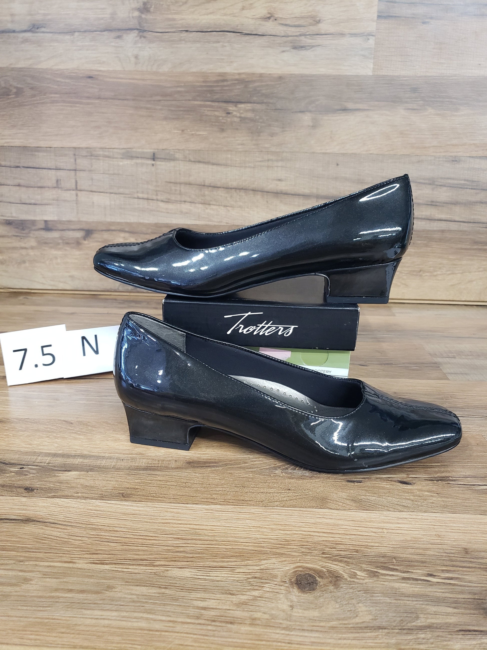Allen's Bootery Doris black pearl patent leather low heel pumps with v-gore detail on a wooden surface