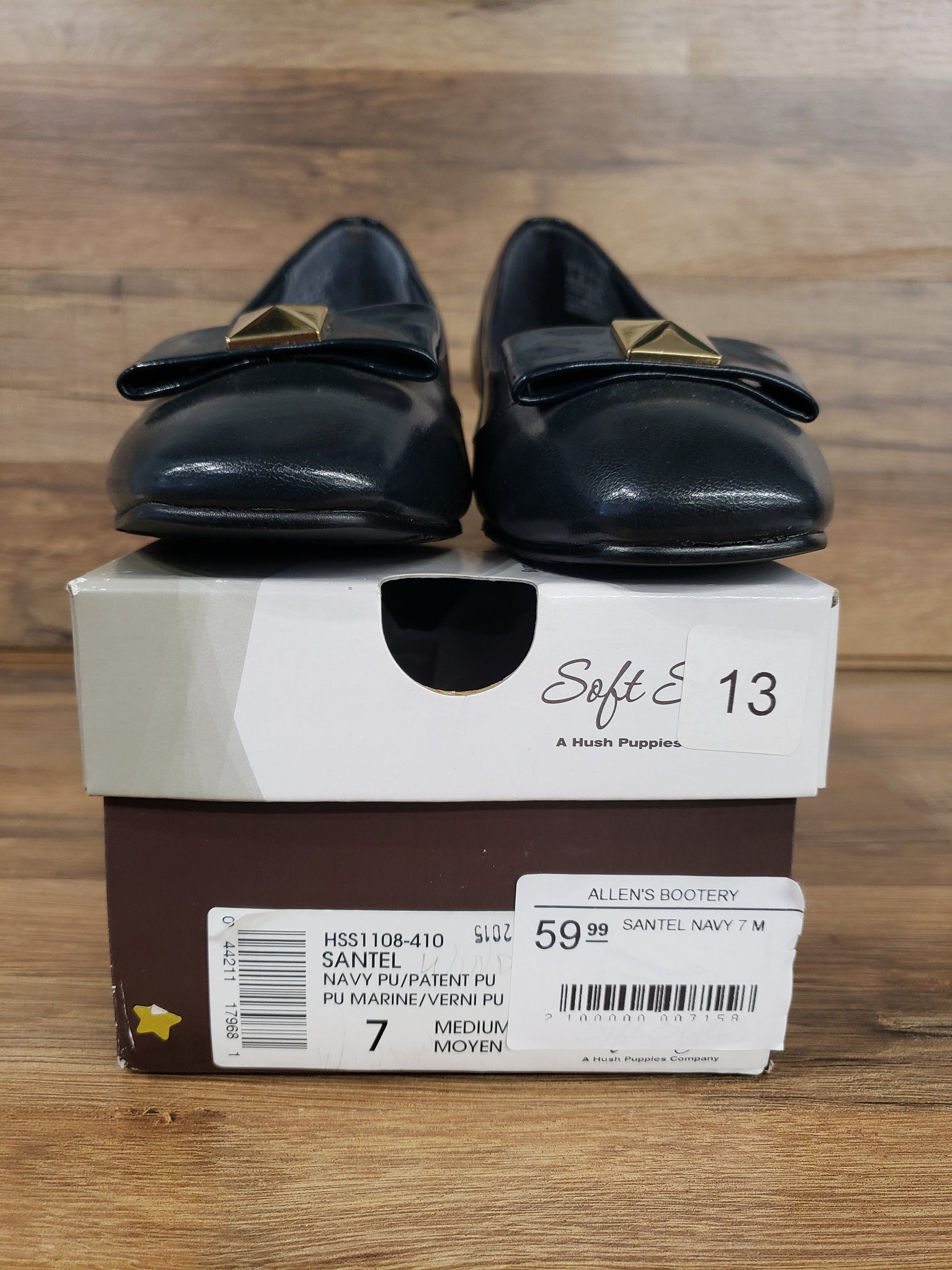 Allen's Bootery navy cap toe pumps with metal ornament and low heel displayed on their original shoe box