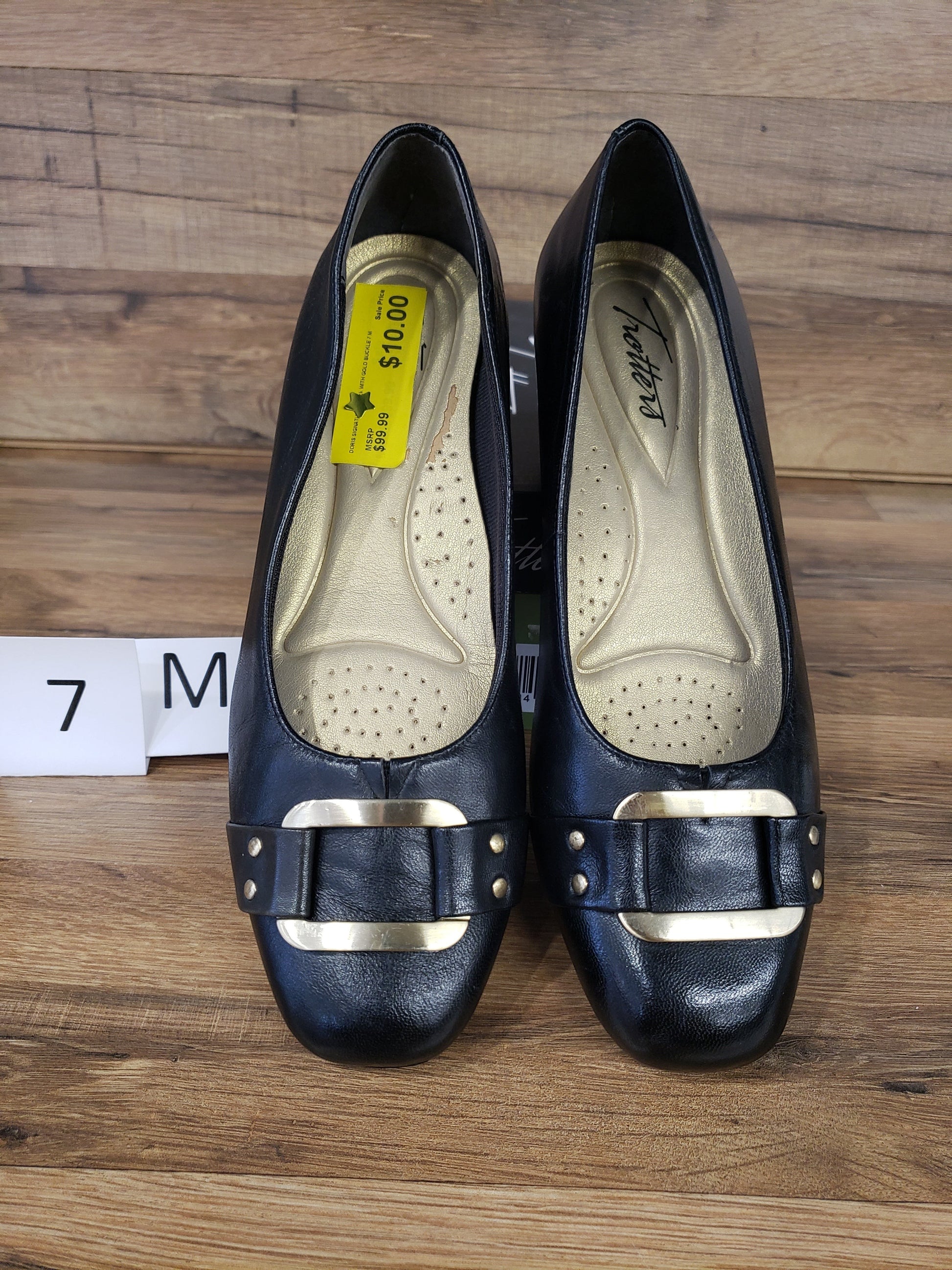Allen's Bootery Trotters Doris Signature black dress shoes with gold buckle and low heel on wood background