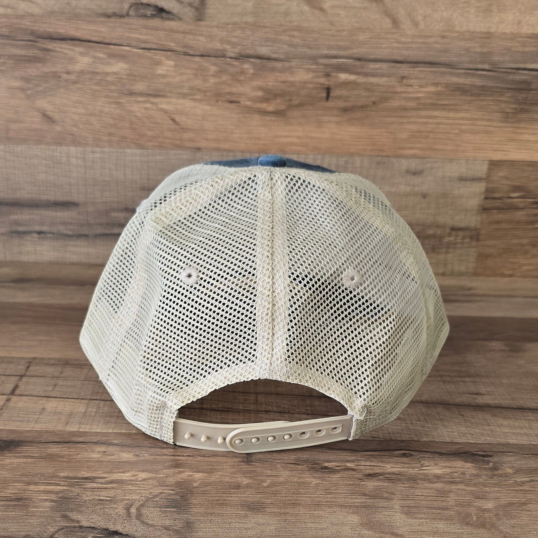 Allen's Bootery trucker hat back view with tan mesh panels and adjustable snapback closure on a wooden background