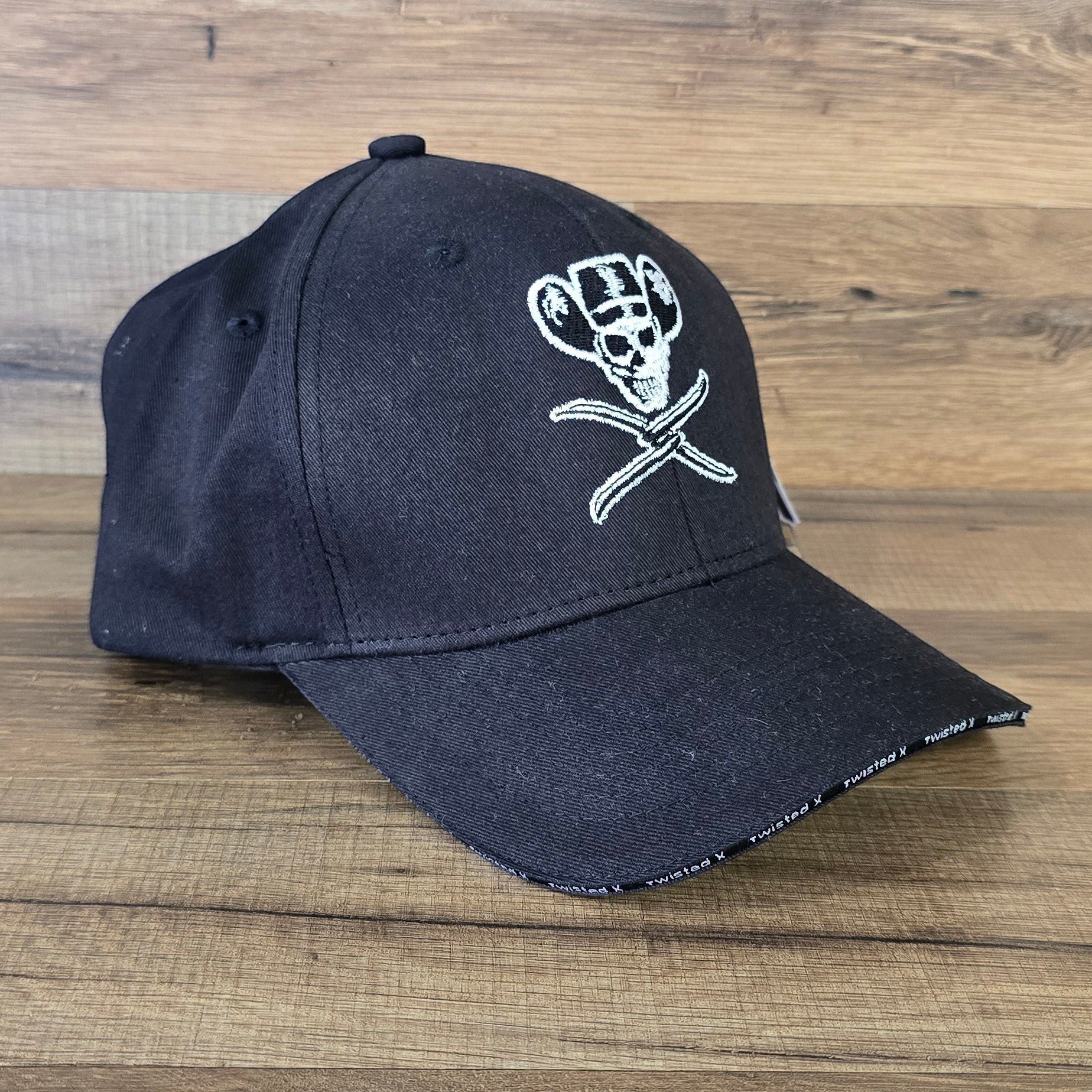 Allen's Bootery black Twisted X baseball cap with white embroidered skull wearing a cowboy hat on a wooden background