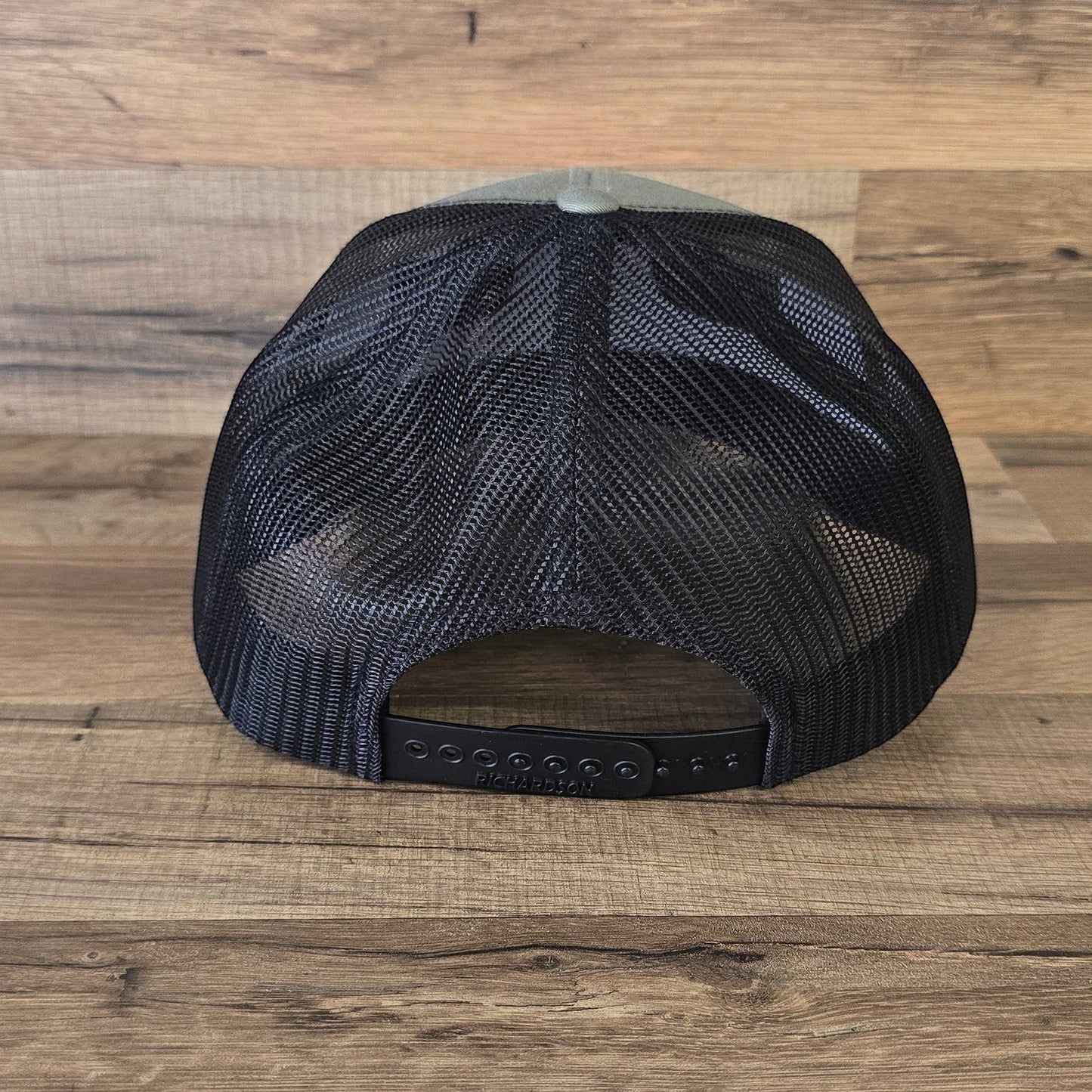 Allen's Bootery Georgia Boot black trucker hat with breathable mesh back and adjustable snapback closure on wood background