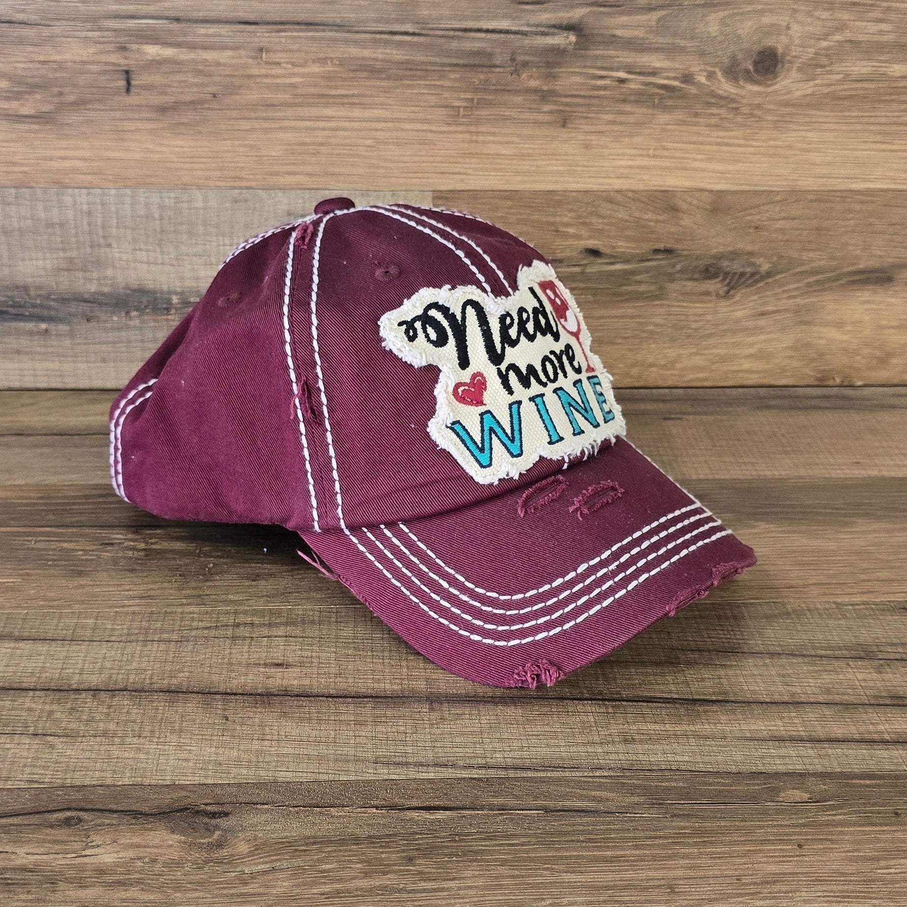 Allen's Bootery burgundy distressed cotton baseball cap with Need More Wine embroidered patch and white stitching.