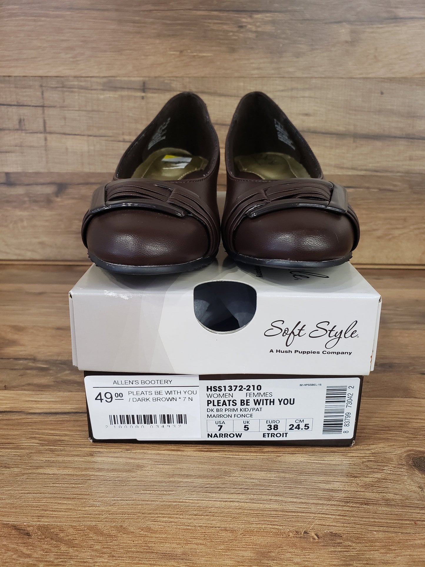 Allen's Bootery dark brown Pleats Be With You closed-toe pumps with a buckled pleat detail and low heel on a shoe box.