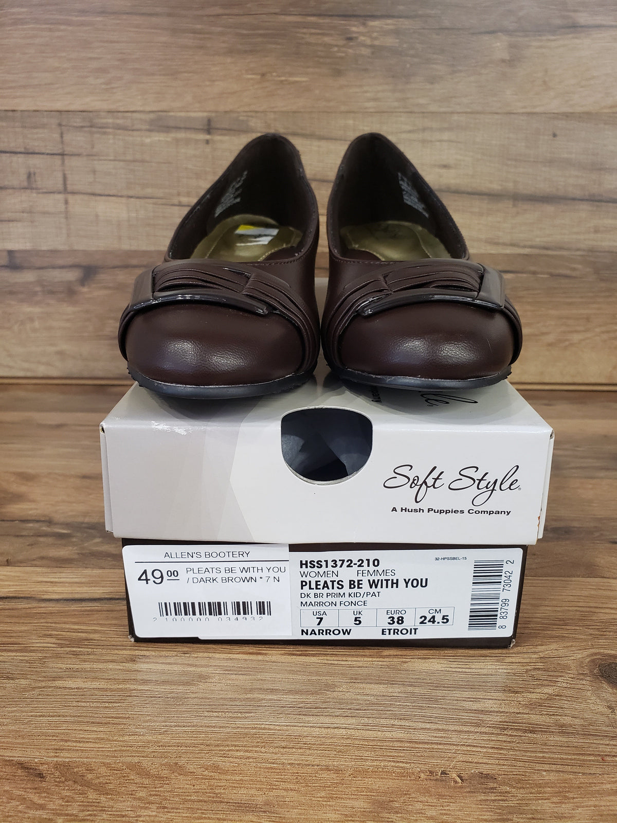 Allen's Bootery dark brown Pleats Be With You closed-toe pumps with a buckled pleat detail and low heel on a shoe box.