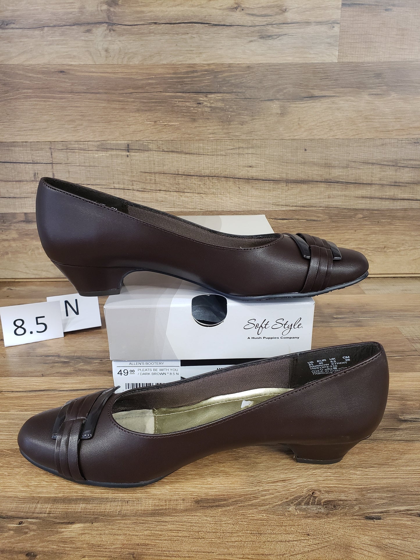 Allen's Bootery Pleats Be With You dark brown round toe pumps with buckle detail and low heels on a wooden surface.