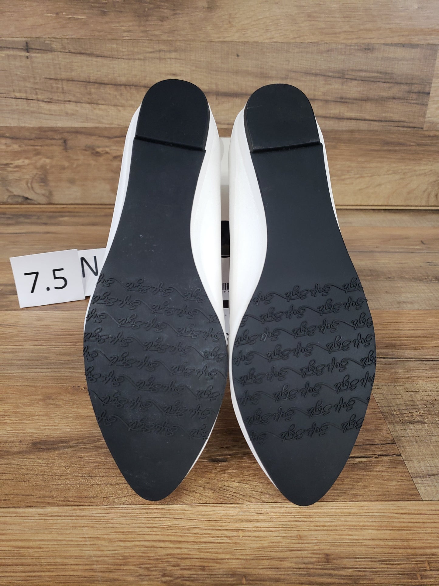 Allen's Bootery Darlene white leather flats showing black synthetic soles with textured grip on a wooden surface