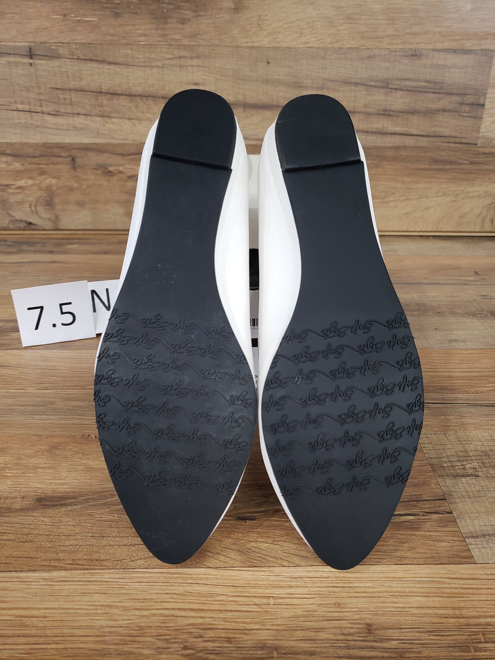 Allen's Bootery Darlene white leather flats showing black synthetic soles with textured grip on a wooden surface
