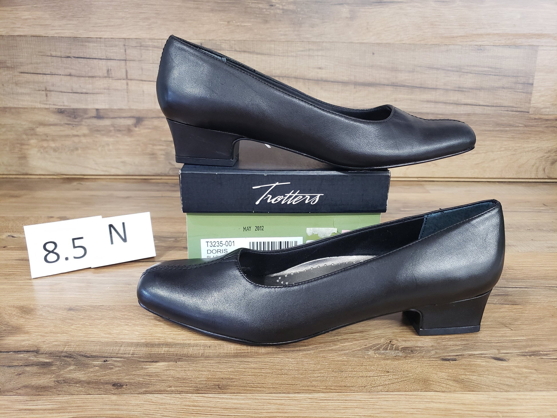 Allen's Bootery Doris black leather low heel pumps with a cushioned footbed and v-gore detail on a wooden background