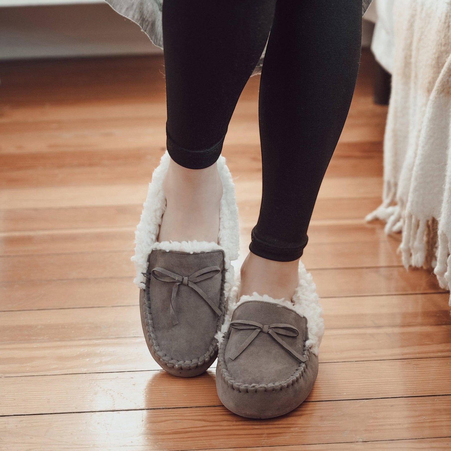 Allen's Bootery Women's grey faux suede moccasin slippers with plush cream faux fur lining and decorative bow.