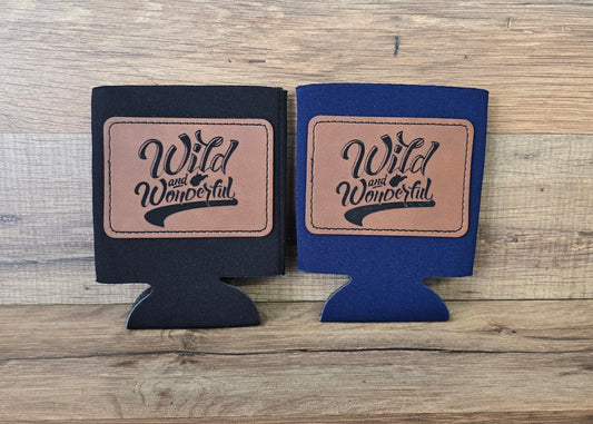 Allen's Bootery Wild & Wonderful foam can koozies in black and navy blue with brown leather patches on a wood background