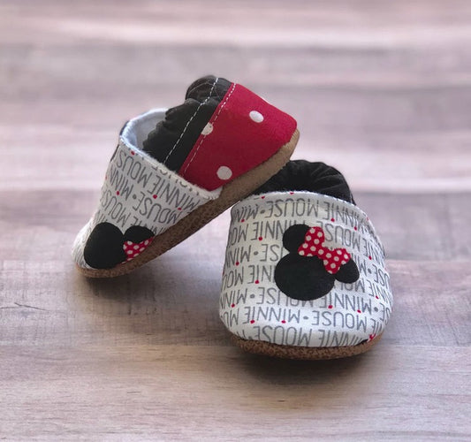 Allen's Bootery soft-soled baby moccasins featuring a white Minnie Mouse print, red polka-dot heel, and black bow.