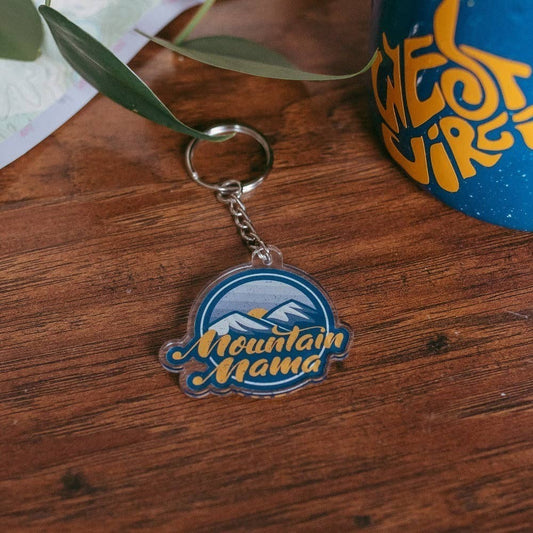 Allen's Bootery Mountain Mama acrylic keychain featuring a blue and yellow mountain graphic on a wooden surface.