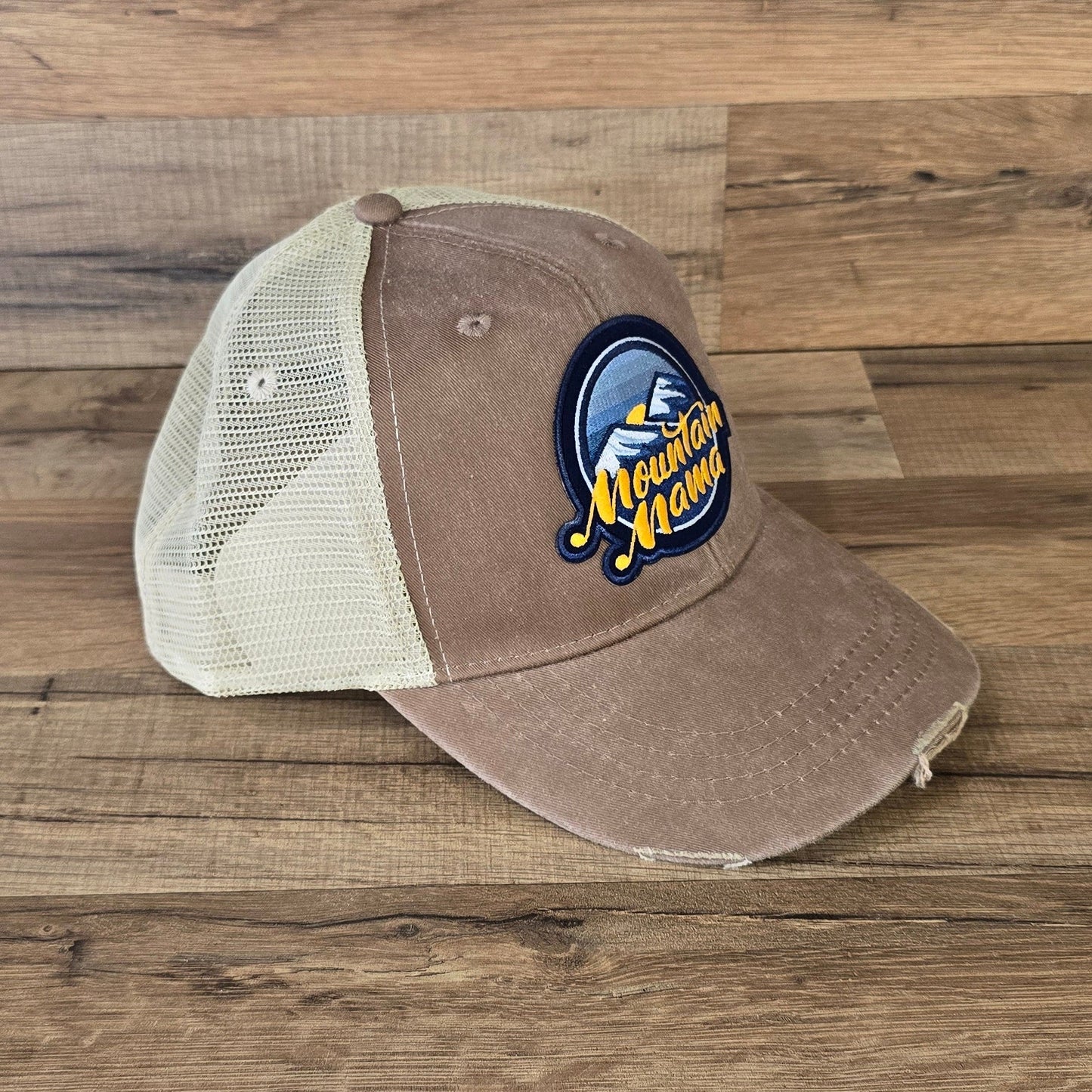 Allen's Bootery Mountain Mama trucker hat with a distressed brown brim, cream mesh back, and mountain landscape patch.