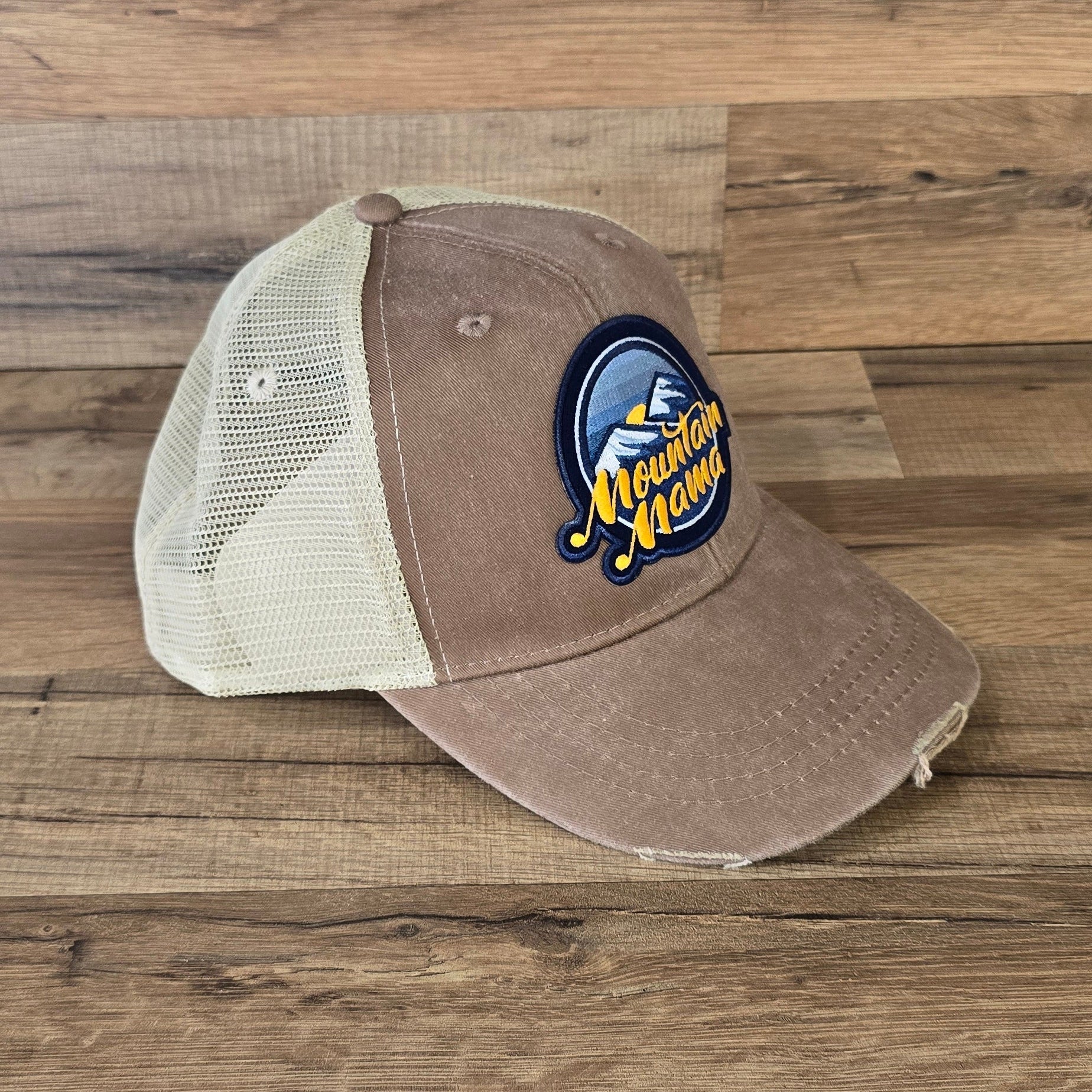 Allen's Bootery Mountain Mama trucker hat with a distressed brown brim, cream mesh back, and mountain landscape patch.