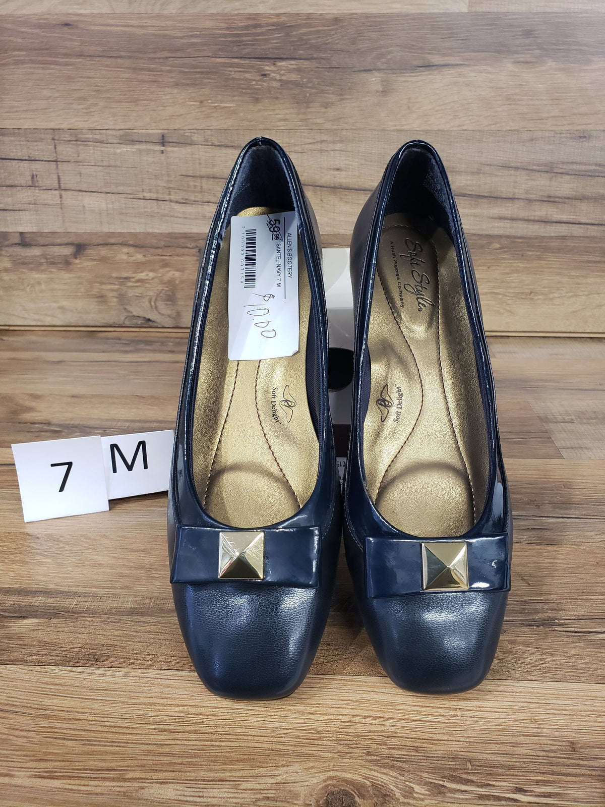 Allen's Bootery navy blue cap toe pumps with gold metal ornaments and low heels on a wooden surface