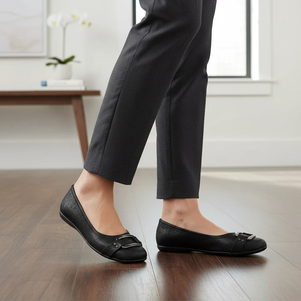 Allen's Bootery Sizzle black ballerina flats with metal buckle detail worn with tailored trousers on a wooden floor