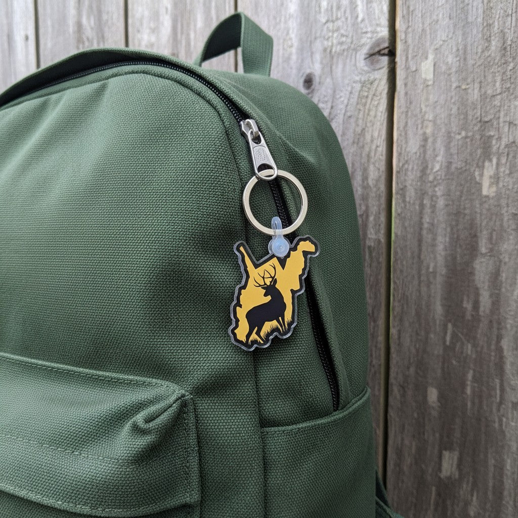 Allen's Bootery West Virginia deer silhouette keychain in gold and charcoal acrylic attached to a green backpack.