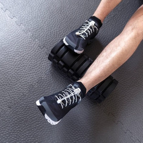 Allen's Bootery white Lock Laces no-tie shoelaces installed on black athletic sneakers on a gym floor
