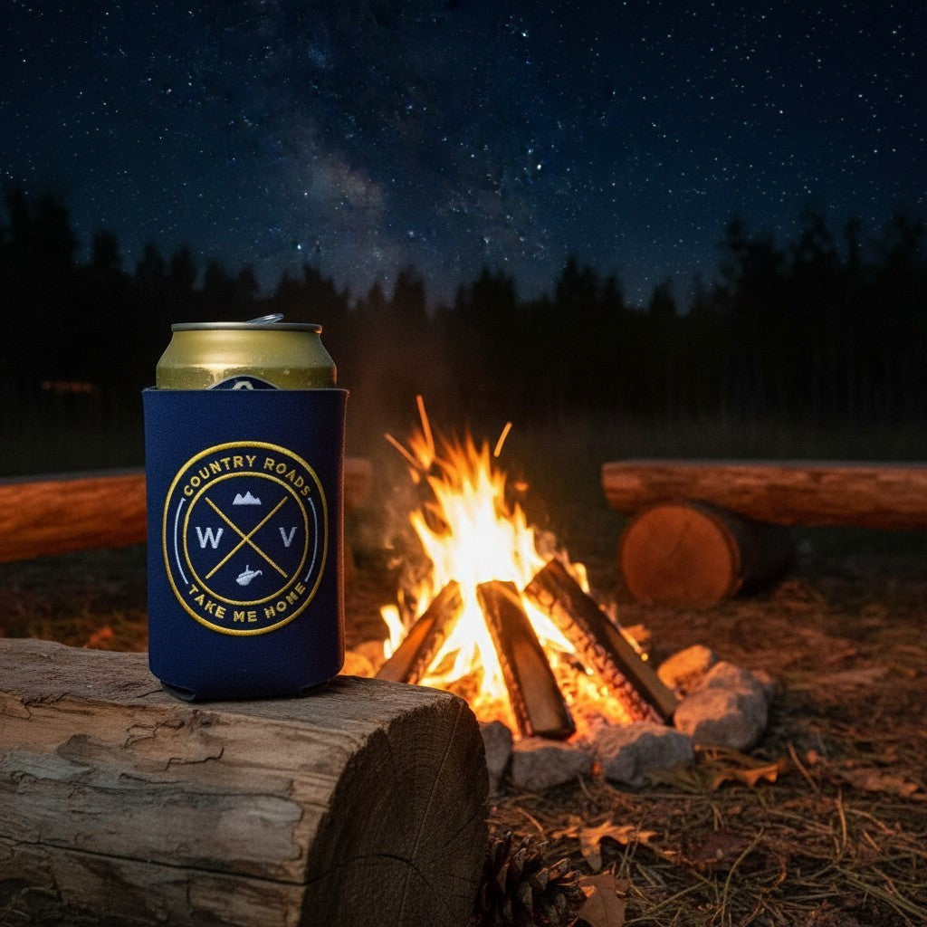 Allen's Bootery navy blue can koozie with embroidered West Virginia seal, sitting on a log by a campfire at night.