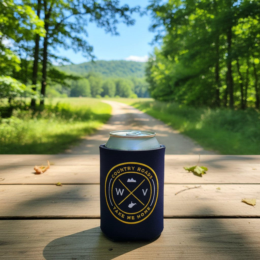 Allen's Bootery WV embroidered neoprene can koozie in blue and gold on a wooden table with a forest path background