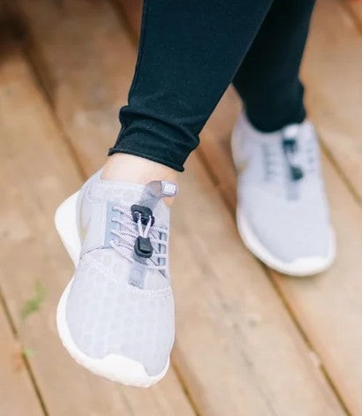 Allen's Bootery Xpand glow-in-the-dark elastic quick-release laces installed on light grey sneakers.