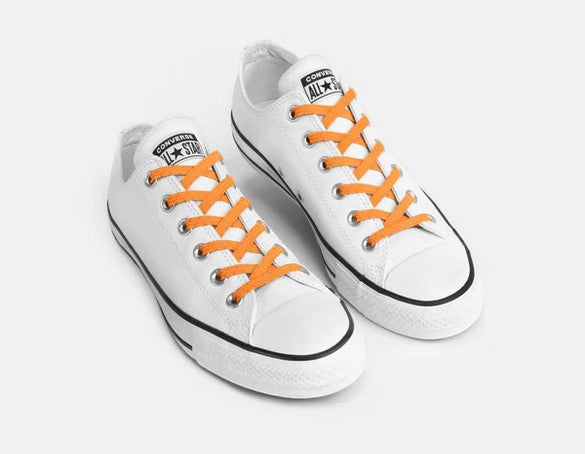 Allen's Bootery Xpand reflective orange no-tie elastic laces installed on white low-top sneakers for a secure slip-on fit.